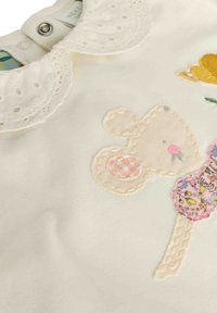 Weißes Kleid aus Stoff mit einem Kragen aus Spitze, gesticktem Mausdesign mit rosa und floralen Akzenten sowie einem metallischen Druckknopfverschluss am Hals.