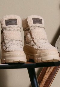 Stivaletti beige con texture, con parte superiore imbottita e suola pronunciata e robusta. Presentano una toppa con logo e un design con lacci incrociati.