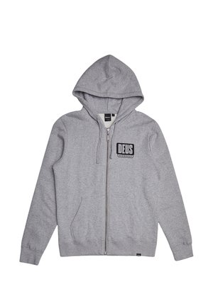 Sudadera con cremallera gris, hecha de tejido suave, con un parche de logo en el frente, capucha con cordón y dos bolsillos laterales. Textura suave en todo el material.