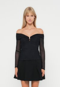 Top noir décolleté avec de longues manches transparentes, tissu froncé au niveau du buste et une petite découpe centrale, agrémenté de deux accents métalliques.