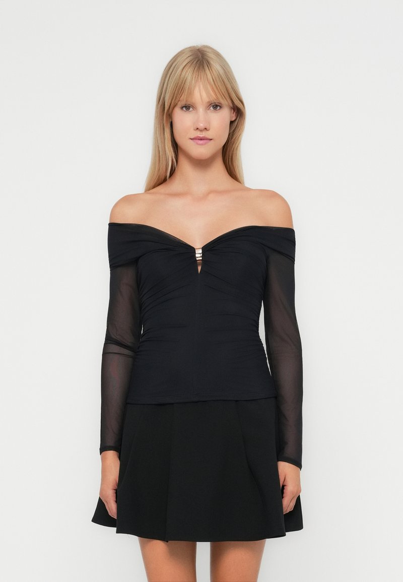 Top noir décolleté avec de longues manches transparentes, tissu froncé au niveau du buste et une petite découpe centrale, agrémenté de deux accents métalliques.