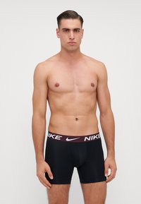 Čierne boxerky s bordo pásom s logom Nike v bielej farbe. Hladká textúra a priliehavý dizajn. Žiadne viditeľné vzory.