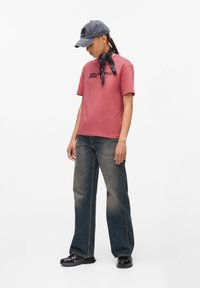 Rausvas medvilninis marškinėliai su "Karl Lagerfeld Jeans" tekstu, derinami su tamsiais džinsiniais plačiais kelnais ir pilku kepurėle. Juoda raštuota skara surišta aplink kaklą.