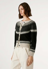 Cardigan à motifs noir et beige avec une fermeture à boutons, texture côtelée et un design en zigzag sur la poitrine et les manches.