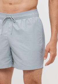 Lichtgrijze zwembroek gemaakt van soepel, snel drogend materiaal. Kenmerkt zich door een elastische tailleband met een trekkoord en zijzakken.