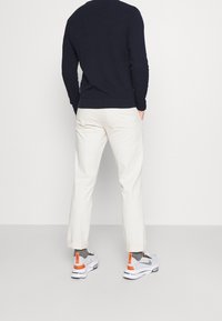 Pull texturé bleu marine, pantalon crème, baskets gris et blanc avec accents orange. La tenue présente une coupe décontractée et des détails visibles.