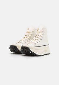 Höga sneakers i off-white kanvas, med en tjock svart gummisula med texturerat grepp, silverfärgade öglor och krämfärgade snören.