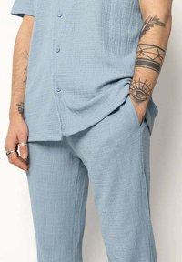 Ensemble deux pièces bleu clair en tissu texturé. Chemise à manches courtes à boutons avec une coupe décontractée et pantalon assorti avec poches.