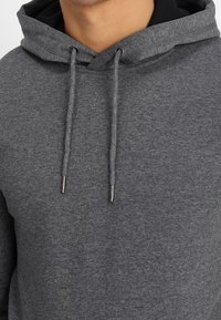 Grijze hoodie van zachte stof met een trekkoordkap, voorzien van metalen punten aan de koorden en een contrasterende zwarte binnenhals.