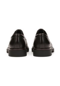 Zapatos de cuero negro con una textura suave, parte trasera redondeada y suelas gruesas de goma negra. Diseño minimalista con detalles de costura sutiles.