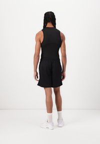 Top atlético negro sin mangas combinado con pantalones cortos negros. El modelo lleva zapatillas blancas y calcetines de longitud crew, mostrando un diseño simple y funcional.