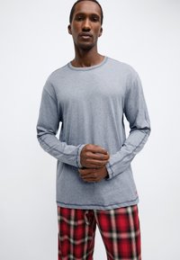 Grå långärmad t-shirt med rund halsringning och kontrasterande sömmar, kombinerad med rödrutiga pyjamasbyxor.