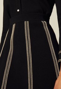 Abito nero lavorato a maglia con corsetto aderente, dettaglio di bottoni in perlone e strisce verticali bianche a contrasto lungo vita e gonna.