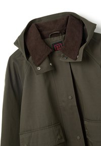 Giacca verde oliva con colletto in corduroy marrone, bottoni a pressione sulla parte anteriore e grandi tasche a patta, esposta appiattita su sfondo bianco.