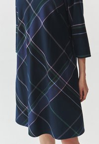 Robe à carreaux marine en tissu doux. Présente une coupe ample avec des manches trois-quarts. Le motif comprend des lignes vertes, roses et blanches.