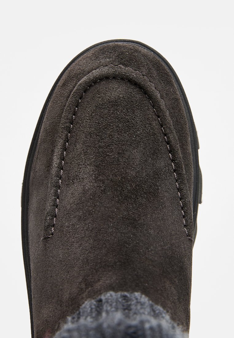 Scarpa slip-on in suede grigio con punta rotonda, cuciture dettagliate lungo il bordo e suola in gomma testurizzata. Nessun abbellimento visibile.