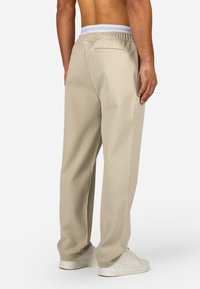 Beige szabadidőnadrág, rugalmas derékkal, hátsó zsebbe és szűkített lábszár dizájnal. Puha anyagból készült, sima tapintással.
