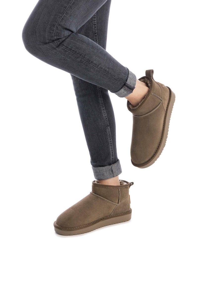 Botines de ante marrón con un forro suave, puntera redondeada y suela de goma baja. Unos jeans de mezclilla remangados completan el look.