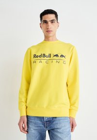Sudadera amarilla de mezcla de algodón, con cuello redondo, mangas largas y un prominente logo negro de "Red Bull Racing" en la parte frontal.
