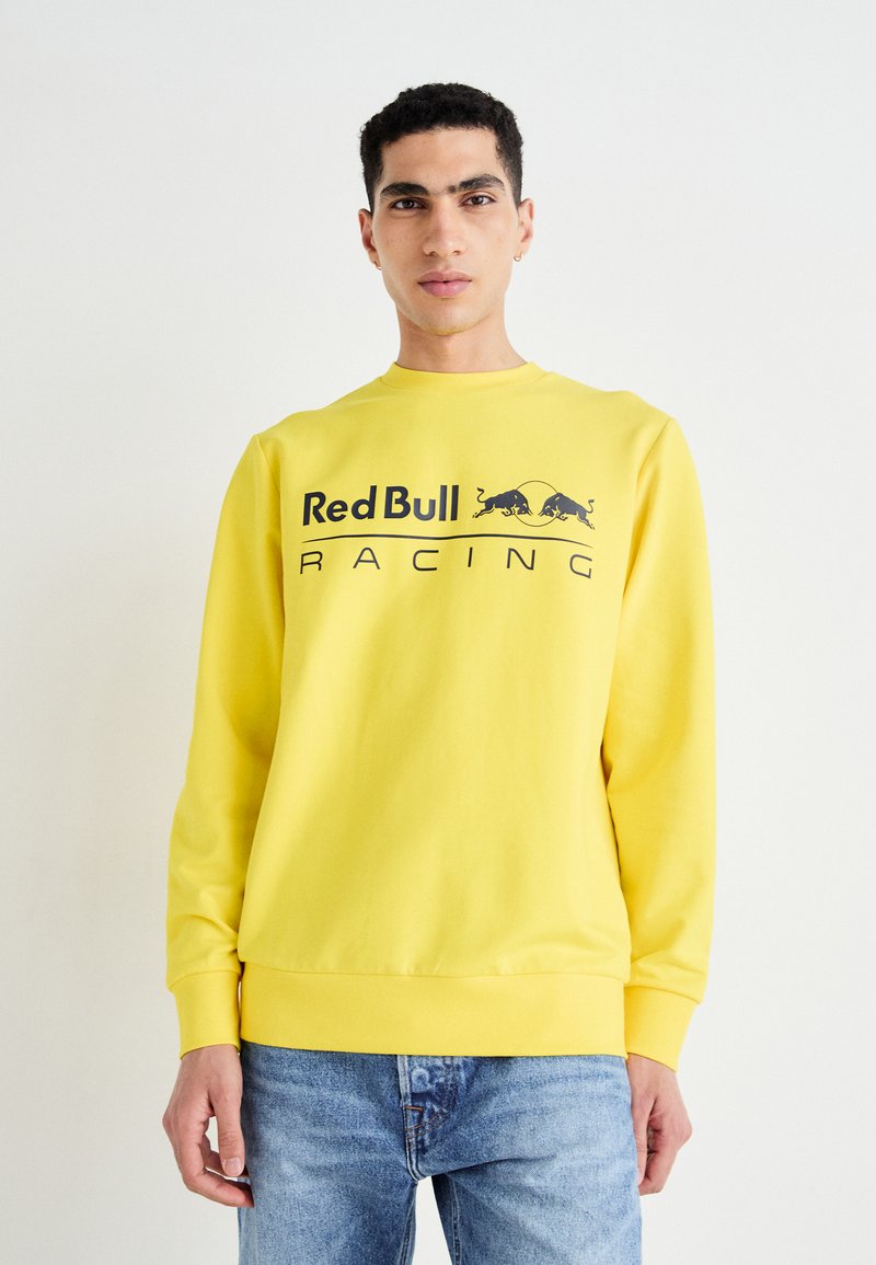 Sudadera amarilla de mezcla de algodón, con cuello redondo, mangas largas y un prominente logo negro de "Red Bull Racing" en la parte frontal.
