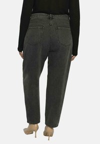 Czarne dżinsy z wysokim stanem, z prostymi nogawkami, pięcioma kieszeniami i subtelnym efektem prania. Noszone z beżowymi szpilkami.