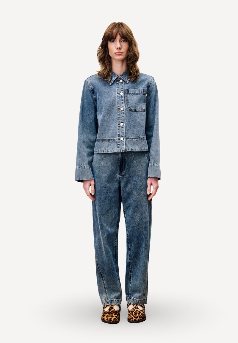 Denim jacket en losse spijkerbroek in lichtblauw, met een knoopsluiting, borstzak en rechte pijpen. Draagt met schoenen in luipaardprint.