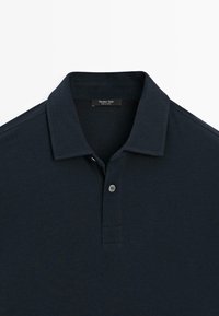 Marinblå polo skjorta med klassisk krage, korta ärmar och en enkel knappslå. Tyget är mjukt och lätt, lämpligt för avslappnad klädsel.