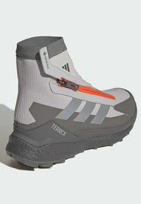 Grå och vit vandringskänga med hög ankelkonstruktion, Gore-Tex-material, orange dragkedjedetalj och texturerad gummisula med Terrex-märkning.
