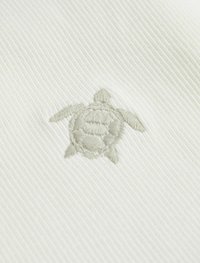 Broderet skildpadde-design på tekstureret hvidt stof. Skildpadden er detaljeret med lys grå syninger mod den ribbede baggrund.