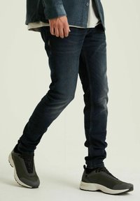 Donkerblauwe denim jeans met een slim fit, gecombineerd met donkergroene en zwarte sportschoenen met textuurpanelen en een dikke zool.