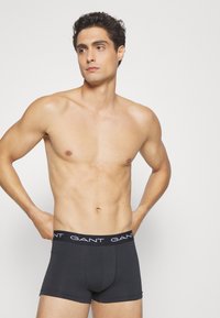 Boxeri negri pentru bărbați, cu o potrivire strânsă, realizati dintr-un material moale, cu un brâu negru și un logo alb. Textură netedă și design minimalist.