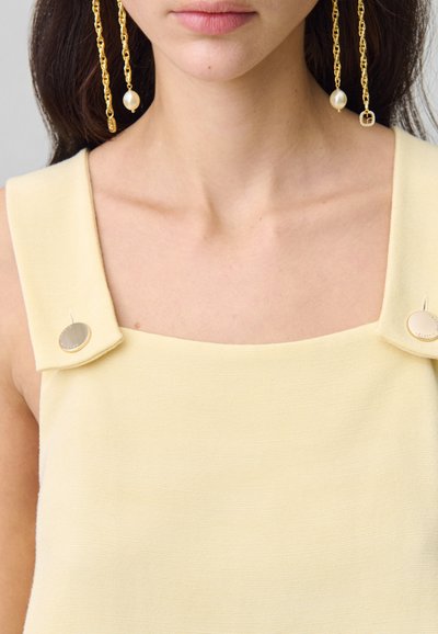 Top giallo senza maniche con tessuto texturizzato, dotato di spalline quadrate e bottoni tondi in tono oro. Il design elegante mette in risalto la semplicità.