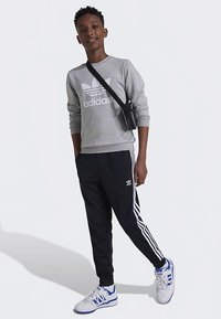 Siva jopa z belim logotipom Adidas, v kombinaciji s črnimi hlačami z belimi stranskimi črtami. Videz dopolnjujejo bele in modre superge.