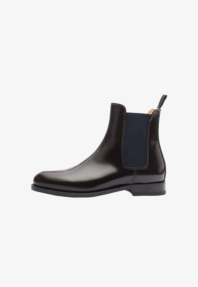 Bota Chelsea negra de cuero con paneles laterales elásticos, punta redondeada y una lengüeta en la parte posterior. Textura suave y suela de goma plana.