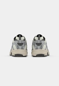 Pair of gray and beige athletic sneakers shown from the back, featuring mesh panels and a pull tab on the heel.