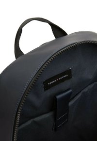 Zaino blu navy con una texture liscia, dotato di maniglia superiore e chiusura con zip. All'interno presenta un'etichetta con il logo e una piccola cinghia per l'organizzazione.