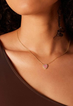 Gold chain necklace featuring a heart-shaped pendant with a pink center and surrounding clear stones, worn on a bare neck.