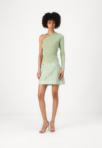 Lichtgroene asymmetrische top met lange mouwen, gecombineerd met een textuurrijke mintgroene tweed mini-jurk. Bevat metallic knopen en heeft een minimalistisch ontwerp.