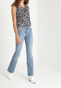 Zwart-witte bloemenprint mouwloze top, gecombineerd met lichtblauwe flared jeans en witte enkellaarsjes met hak en zilveren accenten.