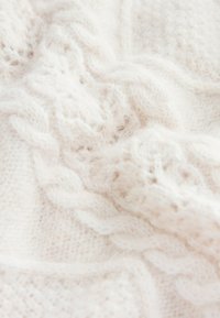 Tela blanca de punto con intrincados patrones de cables y una textura suave y esponjosa. Enfoque en los detalles tejidos y la estructura delicada del hilo.