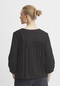Blusa nera con una vestibilità ampia, maniche a tre quarti e schiena arricciata. Il tessuto testurizzato presenta sottili motivi a righe.