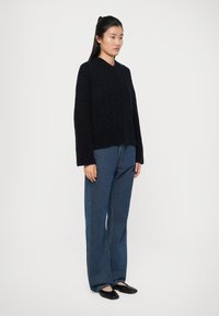 Maglione in maglia blu navy con motivo a zigzag, vestibilità rilassata e maniche lunghe, abbinato a jeans a vita alta con gamba ampia e scarpe basse nere.