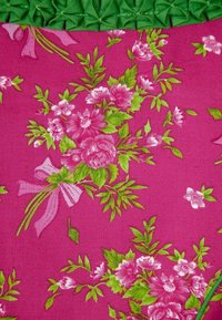 Růžová látka s květinovými vzory v odstínech růžové a zelené, zdobená strukturovaným zeleným lemem nahoře.