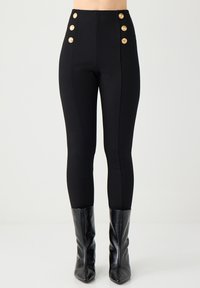 Hochgeschnittene schwarze Hose mit goldenen Knopf-Akzenten am Bund und taillierter Passform. Glattes Gewebe mit leichtem Stretch für Komfort.