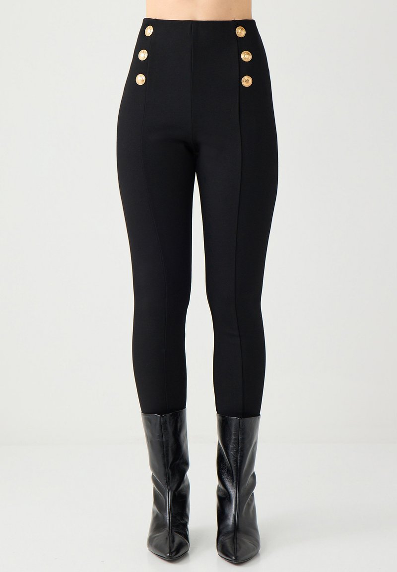 Hochgeschnittene schwarze Hose mit goldenen Knopf-Akzenten am Bund und taillierter Passform. Glattes Gewebe mit leichtem Stretch für Komfort.