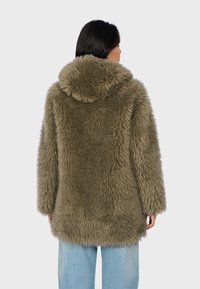 Olive green faux fur coat with a hood, featuring a textured, fluffy exterior and a relaxed fit. Blue jeans visible at the bottom.