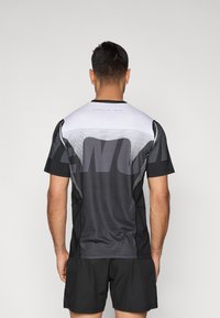 Camiseta desportiva preta apresenta um design em degradê branco com um grande logótipo, textura de rede nos ombros e mangas curtas.