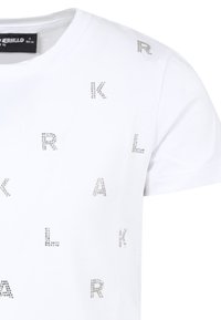 T-shirt en coton blanc avec des lettres en strass argentés disposées de manière sporadique sur le devant. Manches courtes et encolure ronde.