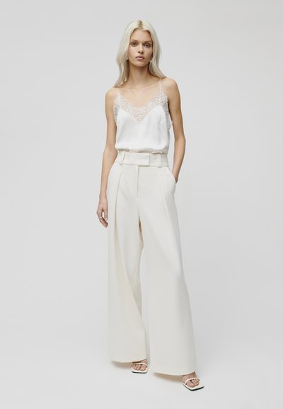Weißes Satin-Camisole mit Spitzenbesatz und hoch taillierten, weiten Creme-Hosen, die ein Gürtel-Design und eine glatte Textur aufweisen.