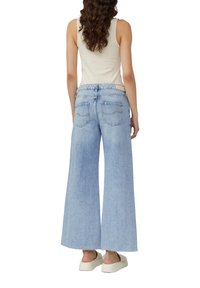 Lichtgewassen, wijde jeans met een ruwe zoom, voorzien van een klassieke 5-pocketontwerp en een middelhoge taille, compleet met een beige tanktop.